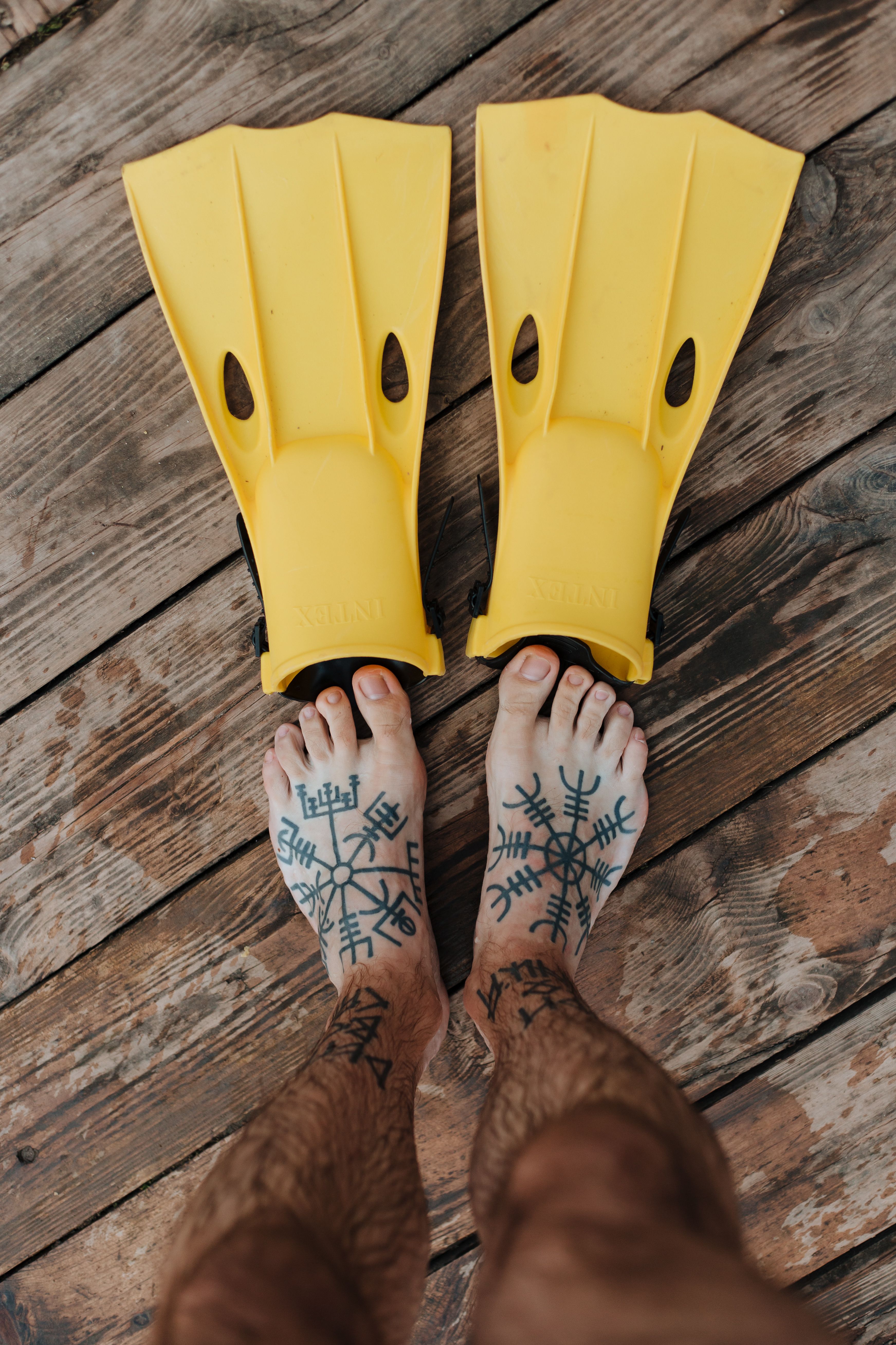 Tatuagem nórdica no pé com sandálias de borracha sobre deck de madeira — verão favorece a cicatrização